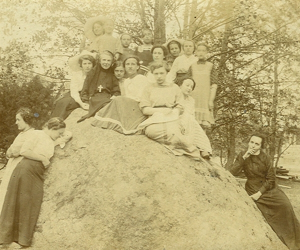 Fotografia przedstawia Urszulę Ledóchowską i grupę uczniów siedzących na dużym głazie. Pozują do zdjęcia. 
